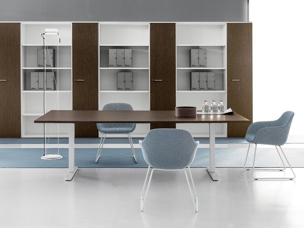 Tavolo da riunione moderno per ufficio con tre sedie blu, su uno sfondo di scaffalature bianche e in legno scuro.