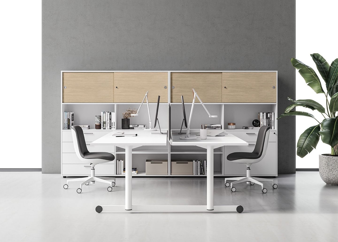 Una moderna postazione di lavoro con scrivania bianca a doppia faccia, armadietti color legno, due sedie con rotelle e una grande pianta in vaso.