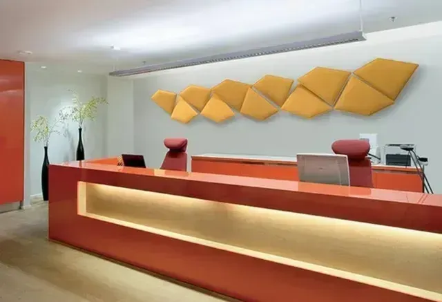 Banco reception moderno di colore arancione in un ufficio luminoso con pannelli decorativi a parete di colore giallo e motivi geometrici.