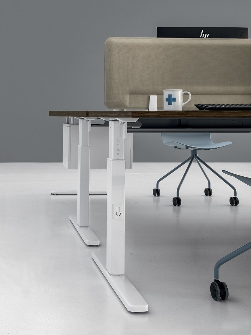 Vista laterale di una scrivania da ufficio bianca, regolabile in altezza, con piano marrone e pannello divisorio acustico beige per garantire la privacy.