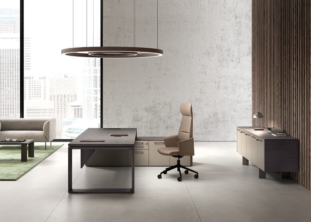 Moderno ufficio direzionale con scrivania, poltrona in pelle, mobile contenitore laterale, divano e lampada a sospensione circolare.