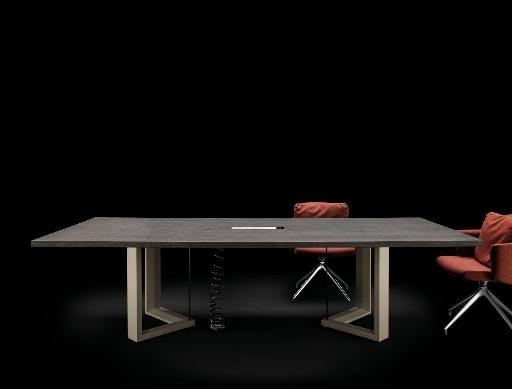 Un elegante tavolo da conferenza grigio con gambe geometriche in metallo e due moderne sedie girevoli color ruggine su uno sfondo nero.