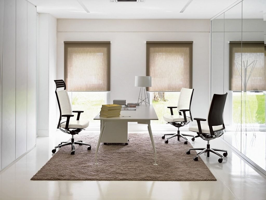 Un ufficio moderno e minimalista con scrivania bianca, tre sedie da ufficio girevoli e un tappeto marrone in una stanza luminosa.