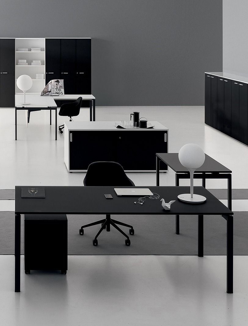 Un moderno interno d'ufficio caratterizzato da diverse scrivanie, sedie da ufficio e unità di archiviazione minimaliste in bianco e nero.