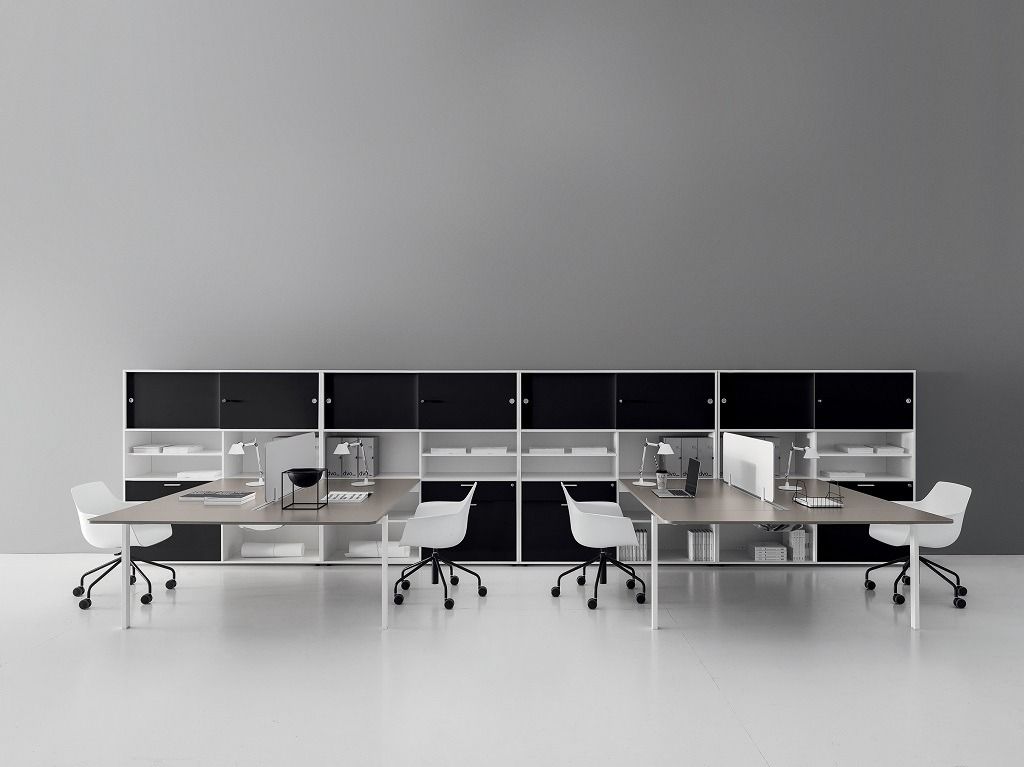 Postazioni di lavoro moderne per ufficio con sedie bianche, scaffalature nere e una parete grigia a contrasto.