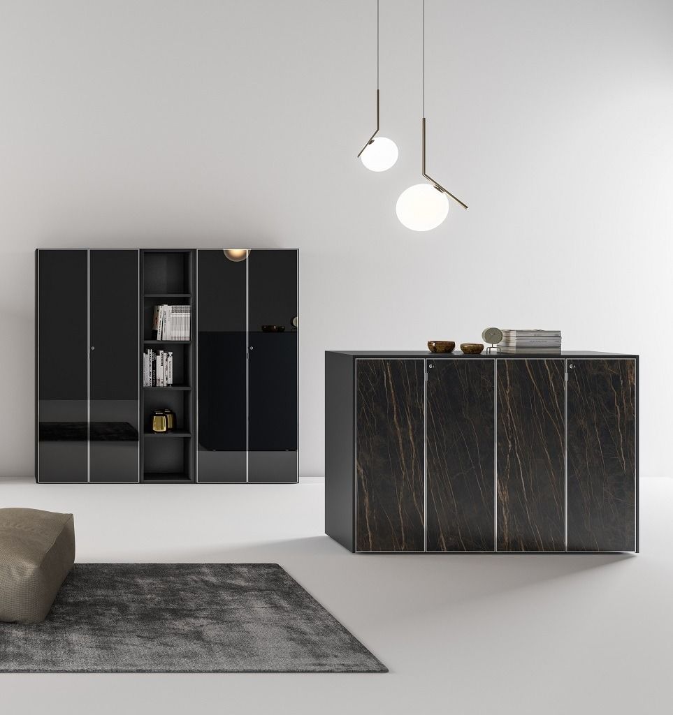 Una stanza moderna con una libreria scura, un mobile con una superficie ruvida, un tappeto grigio e lampade a sospensione a forma di globo su pareti bianche.