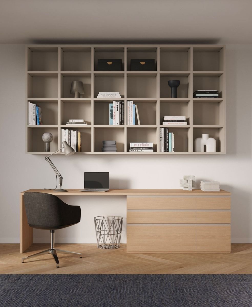 Un ufficio domestico con scrivania e computer portatile, sedia scura, cestino in metallo e una grande libreria in legno a muro.