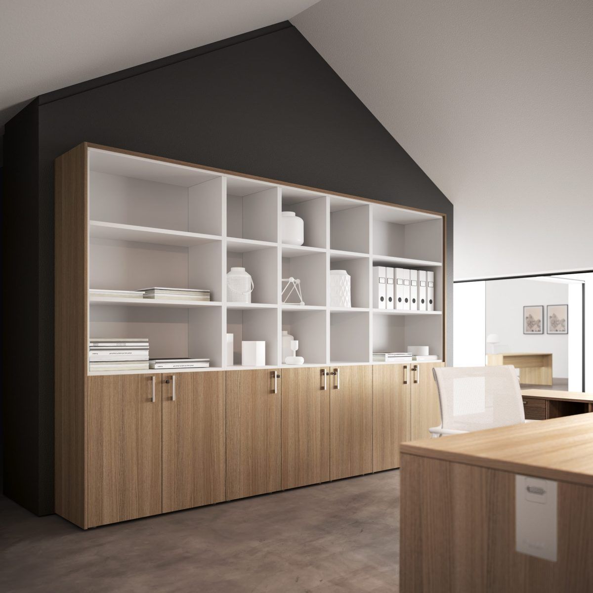 In un ufficio, un mobile contenitore alto in legno con ripiani a giorno e armadietti chiusi è addossato a una parete scura e inclinata.