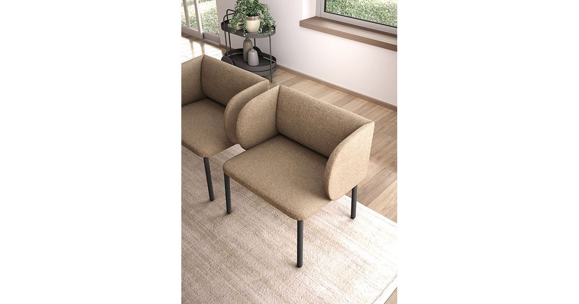 In una stanza minimalista, accanto a un tavolino, due moderne poltrone rivestite in tessuto color cuoio con gambe in metallo scuro sono posizionate su un tappeto.