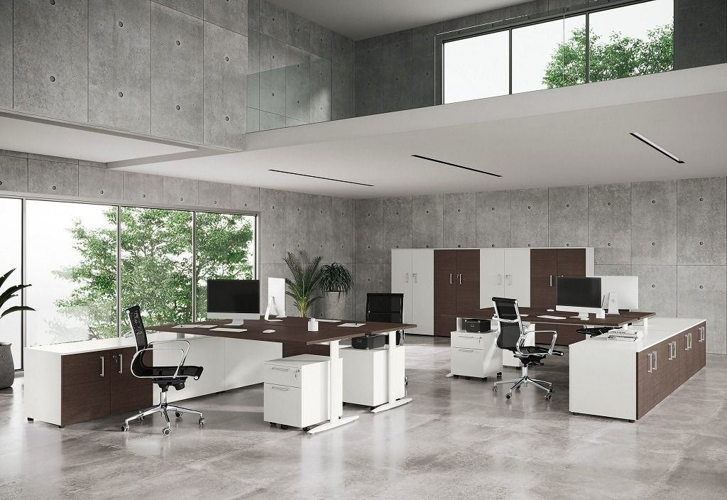 Ufficio moderno con scrivanie angolari in legno bianco e scuro, sedie con rotelle e armadietti in un ambiente open space.