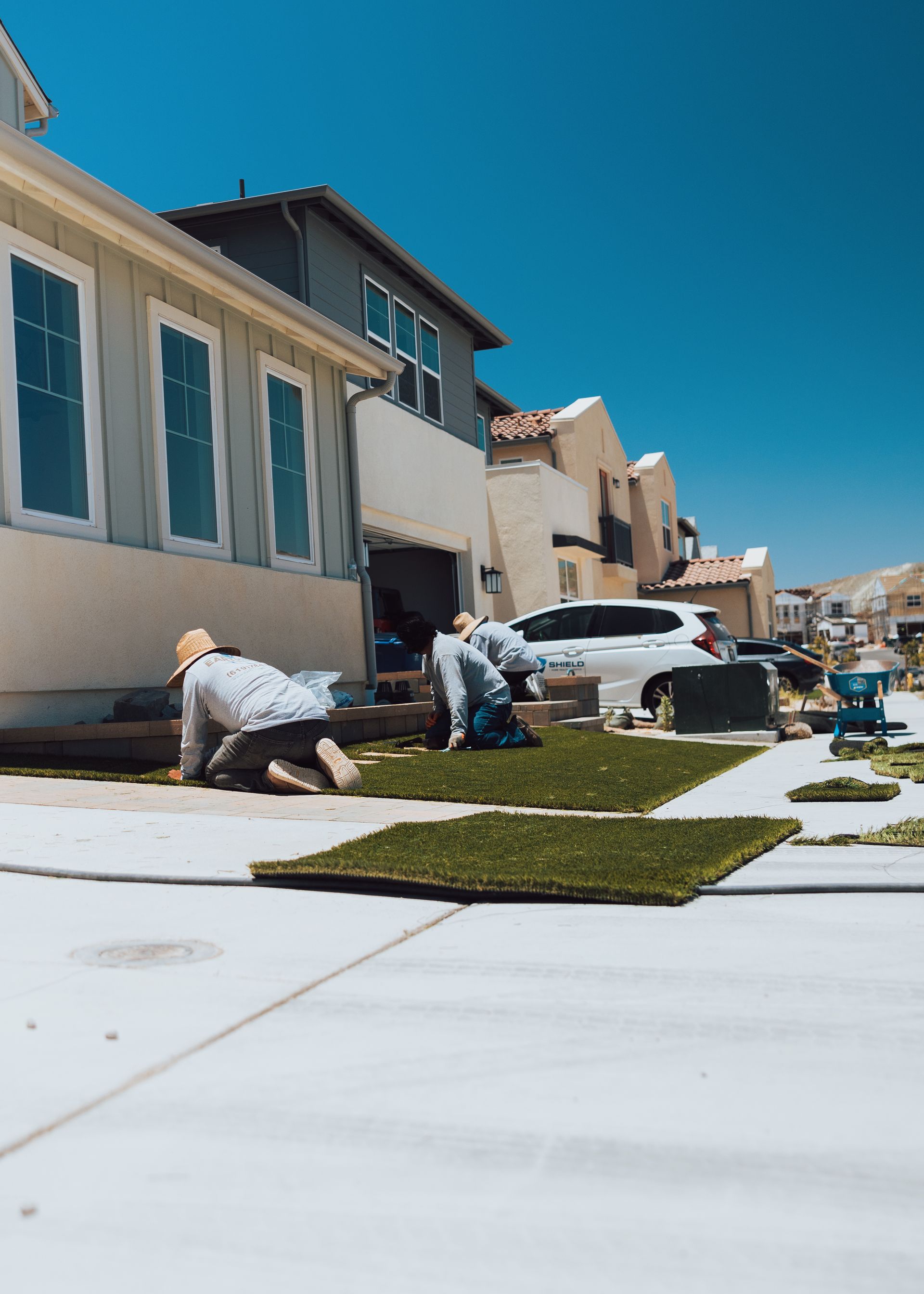 EarthView Landscape team installing artificial turf in a sunny San Diego backyard to replace natural grass