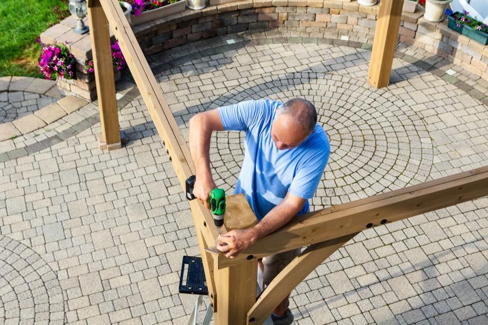 A Man Is Working on A Wooden Structure on A Patio — Bundy Tiny Homes and Carports in Branyan, QLD