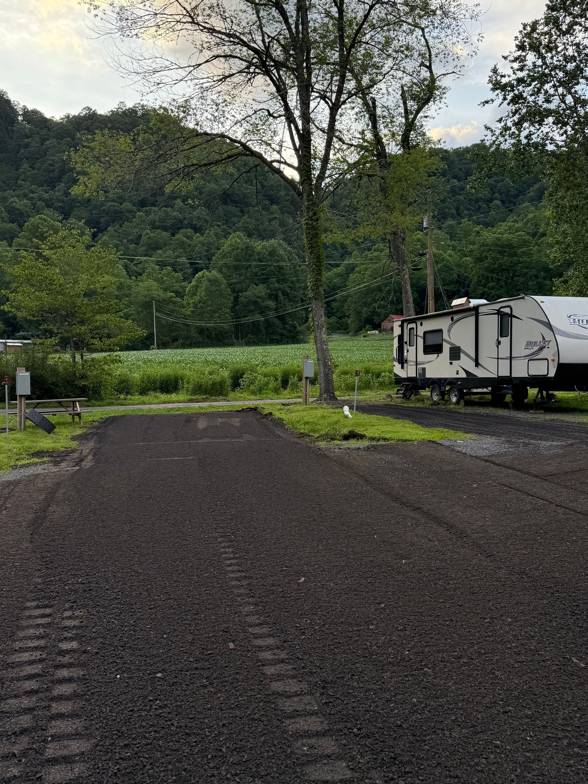 RV parked on gravel lot with a view of a mountain and trees.