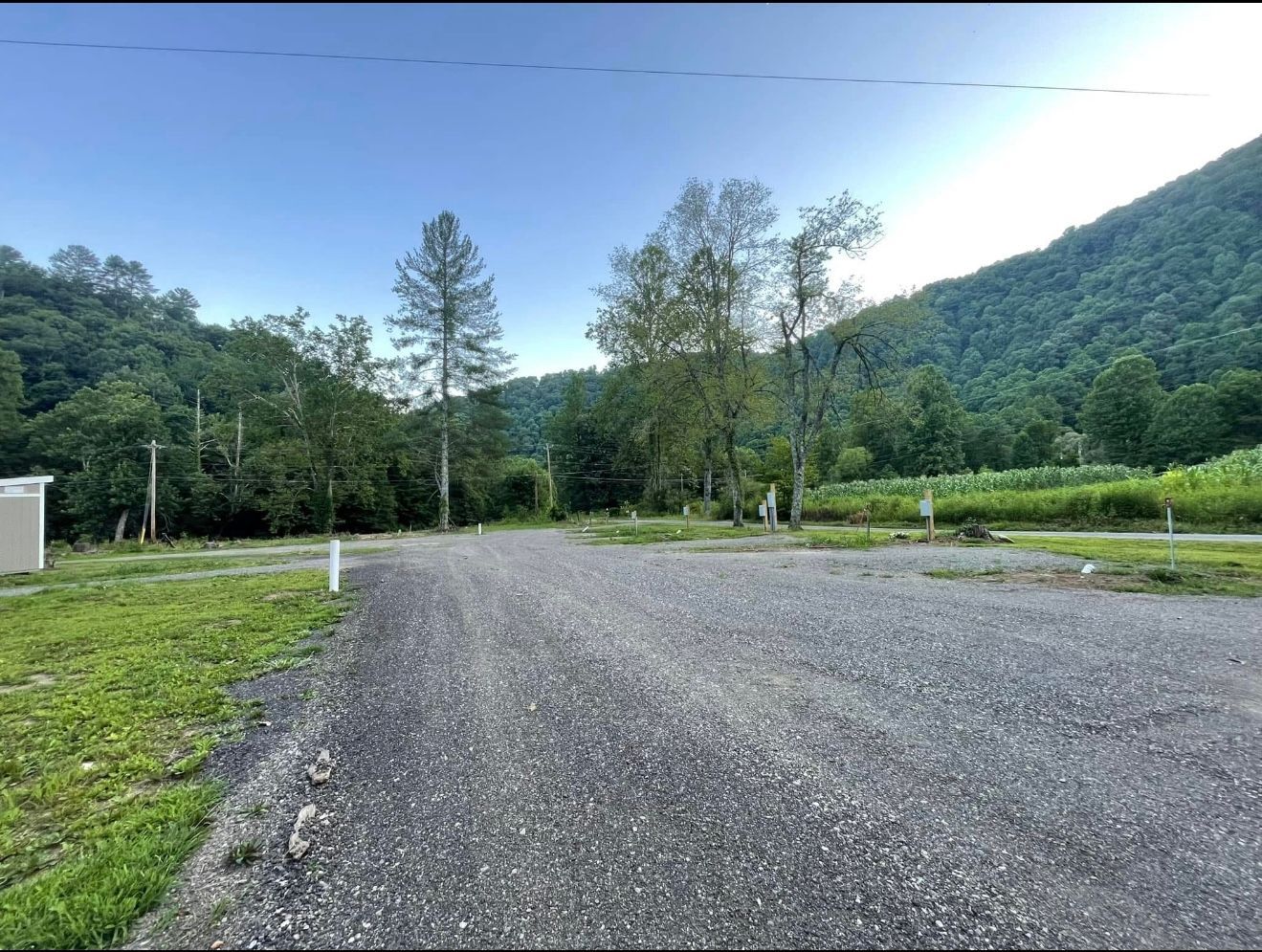 Gravel driveway with trees and mountains in the background under a blue sky.