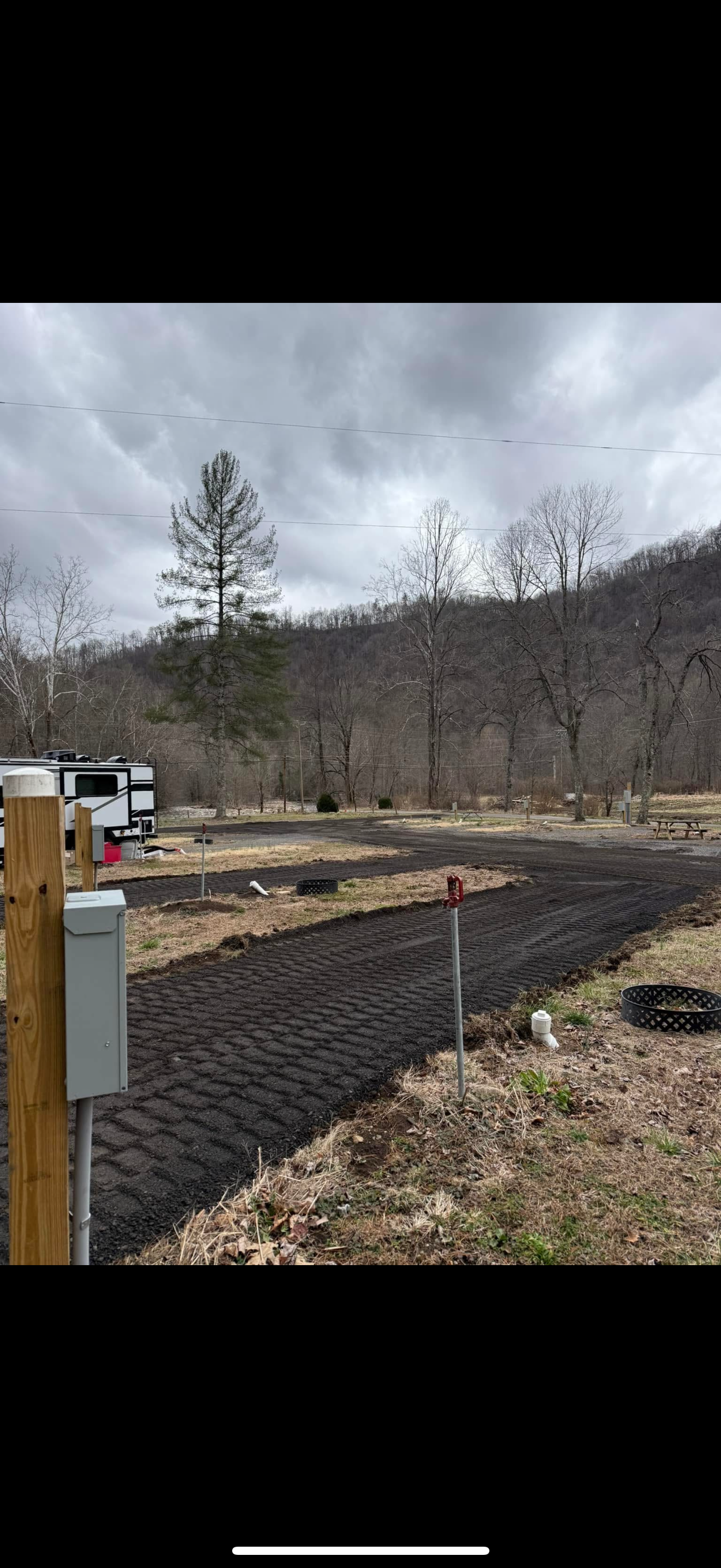 A dirt driveway leads to an RV, with trees in the background under a cloudy sky.