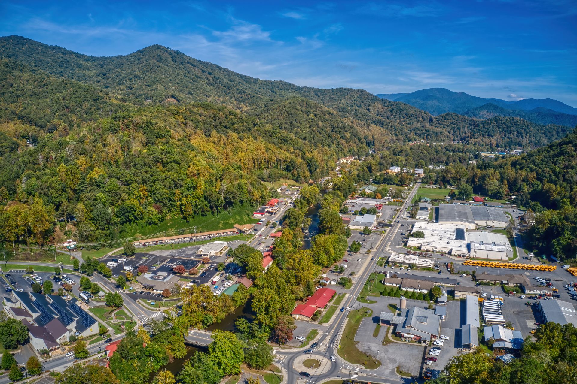 Aerial view of a town nestled in a valley with forested mountains under a clear blue sky.