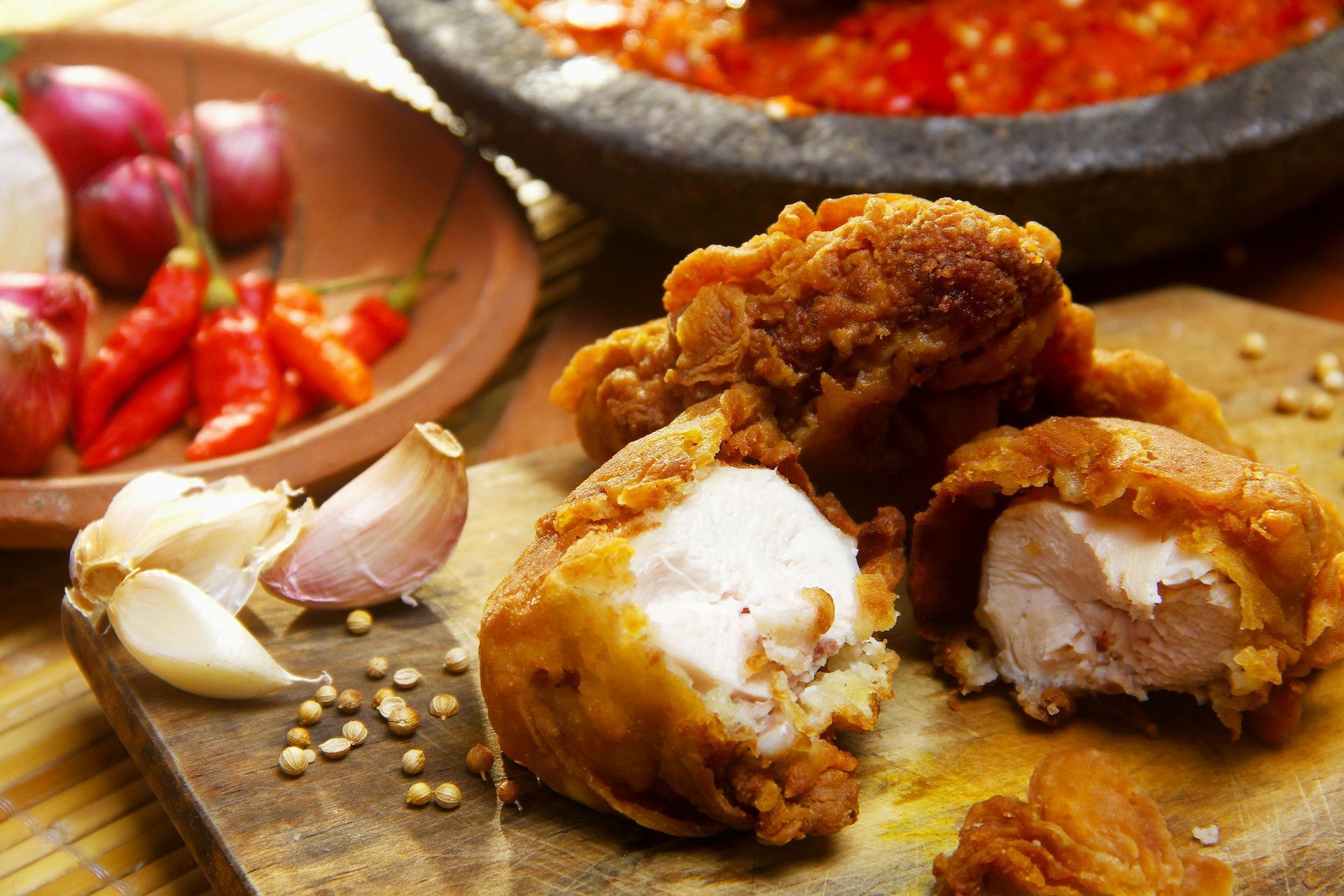 Fried chicken with ingredients: chili, garlic, shallots, and chili sauce in a mortar.