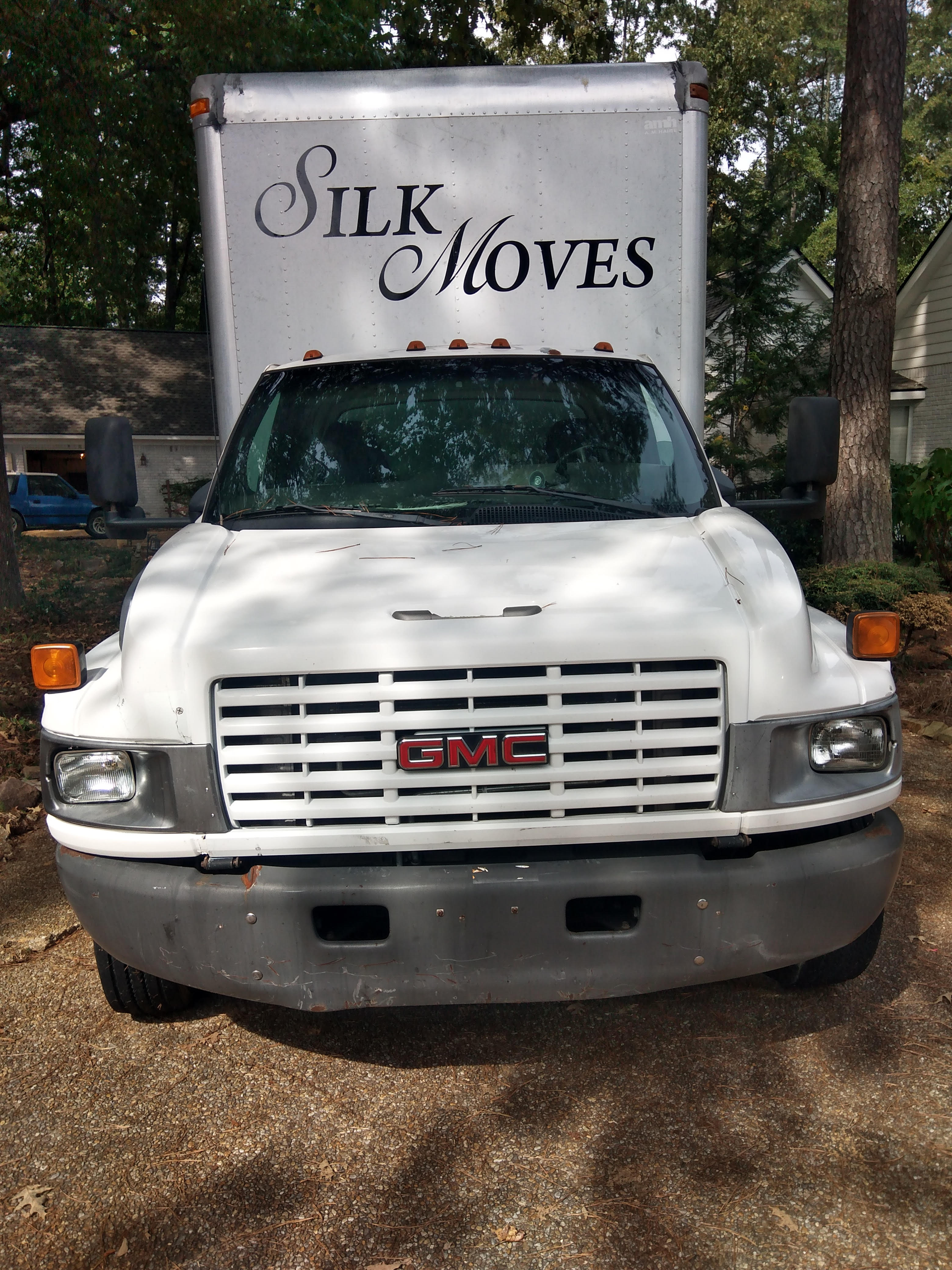 A white gmc truck with a sign that says silk moves is parked in a driveway.
