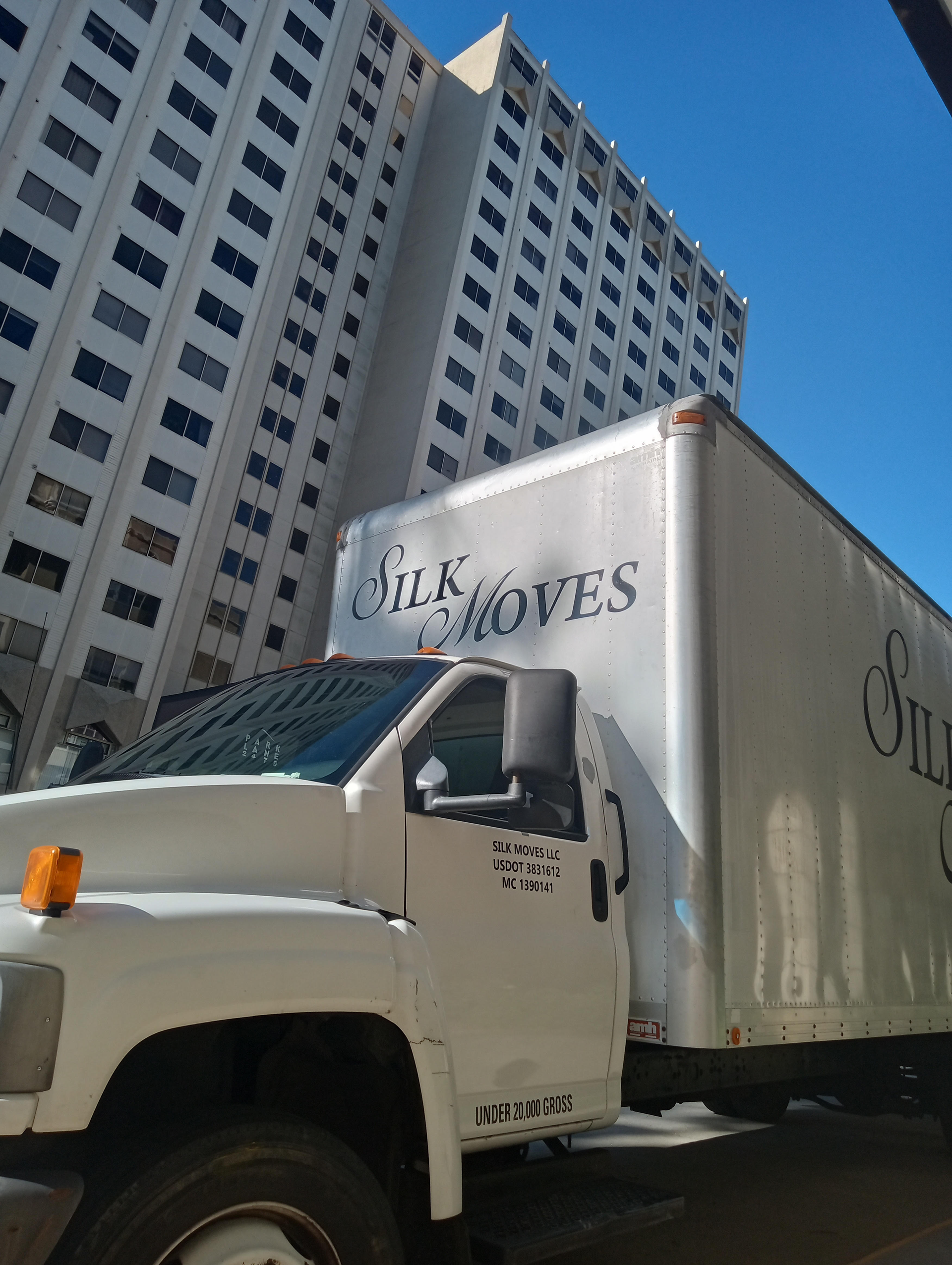 A white moving truck is parked in front of a tall building.