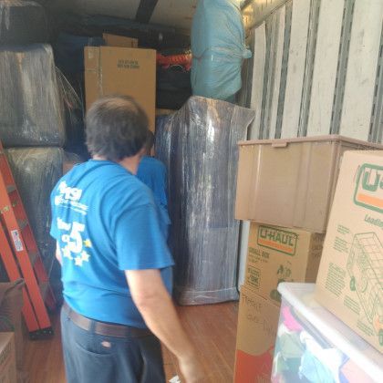 A man in a blue shirt is standing in a room filled with boxes.