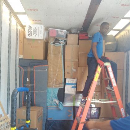 A man standing on a ladder in front of a stack of cardboard boxes with a box that says skechers on it