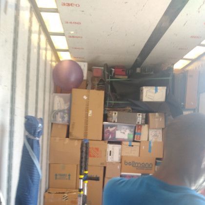 A man is standing in the back of a moving truck filled with boxes.