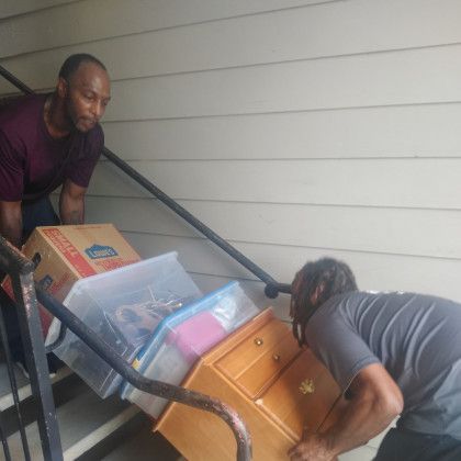Two men are carrying boxes and a dresser up a set of stairs.