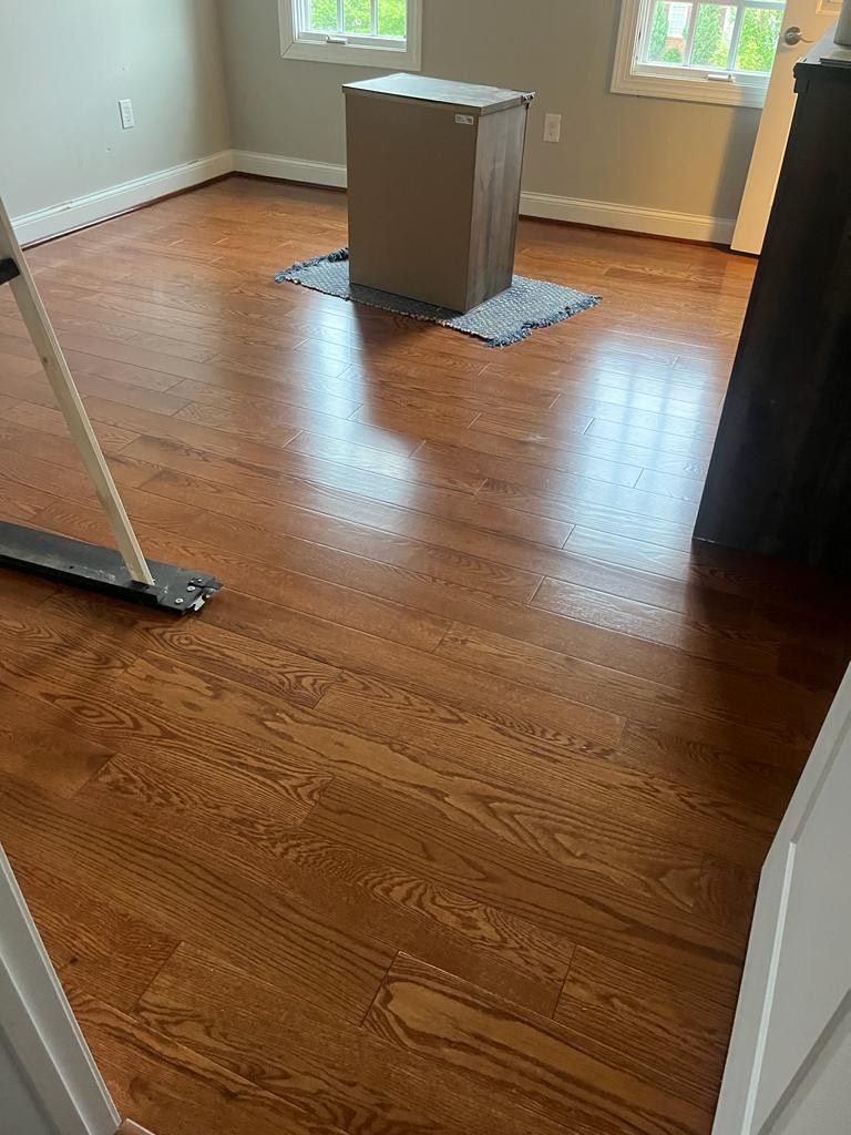 Hardwood floor in a room with a tall box on a mat, a wall, and a wheeled object.