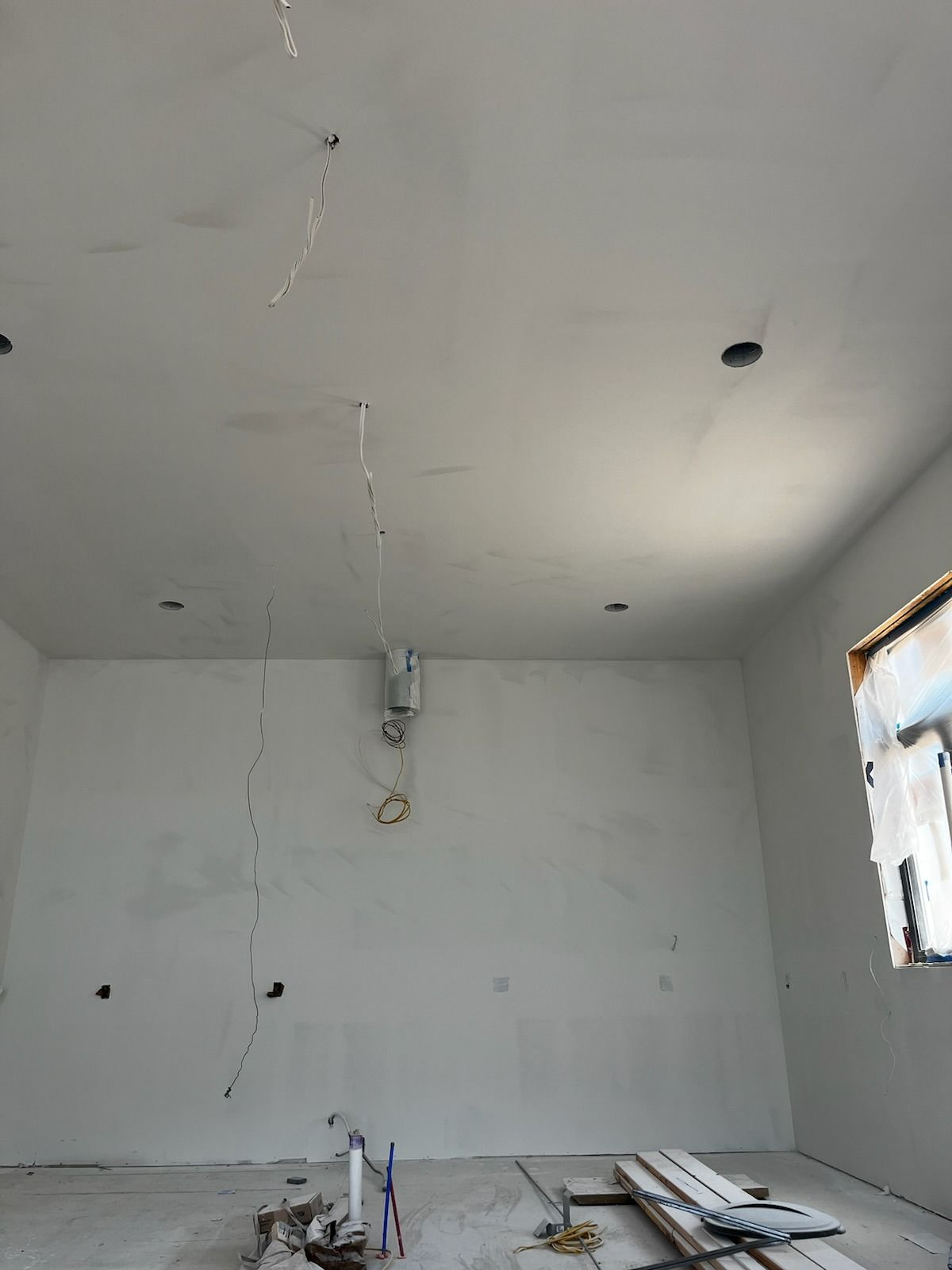 Unfinished interior room with gray walls and ceiling, visible electrical wiring, and a small window.