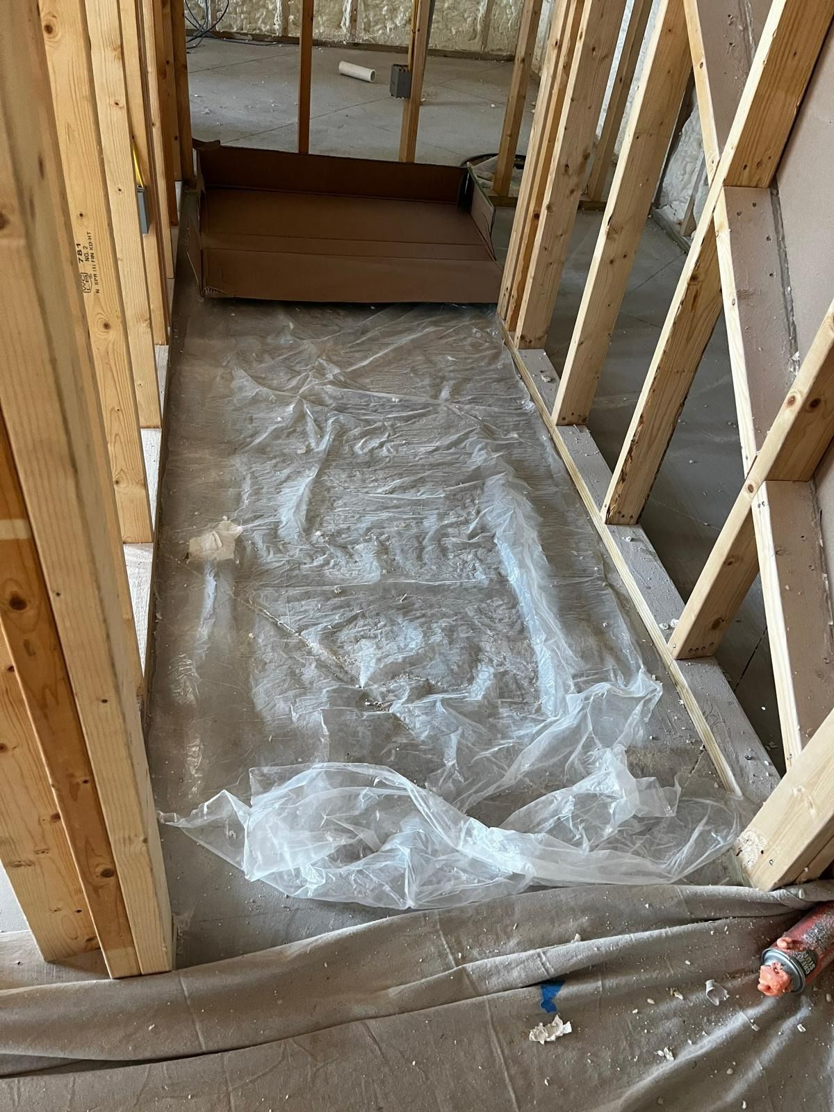 Construction site hallway with wooden frames and plastic sheeting on the floor for protection.