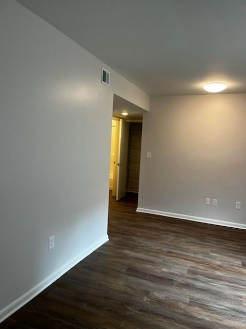 Empty room with dark wood floor, white walls, and a doorway leading to a hallway.