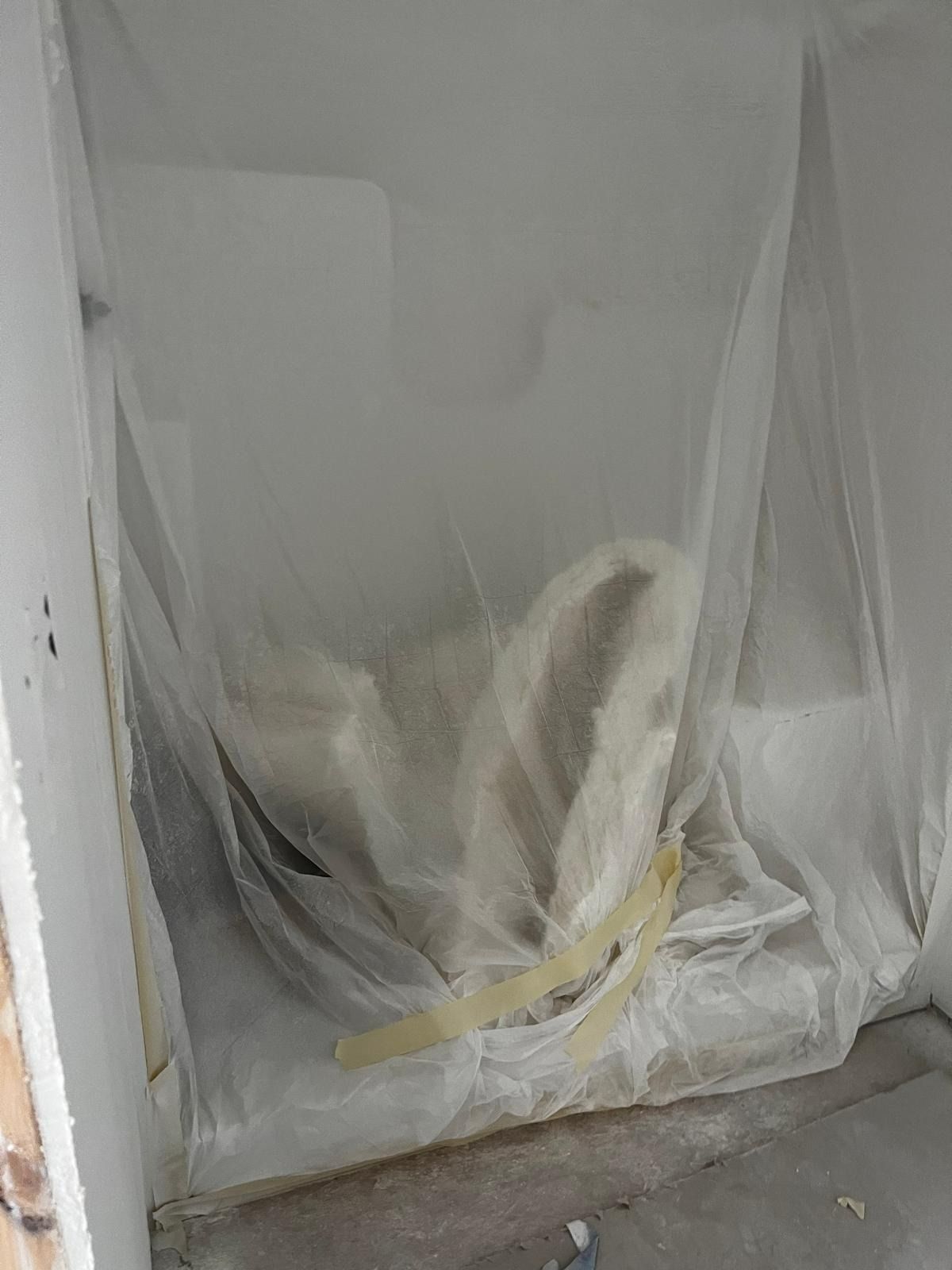 A dusty white room with a toilet covered in plastic, being renovated.