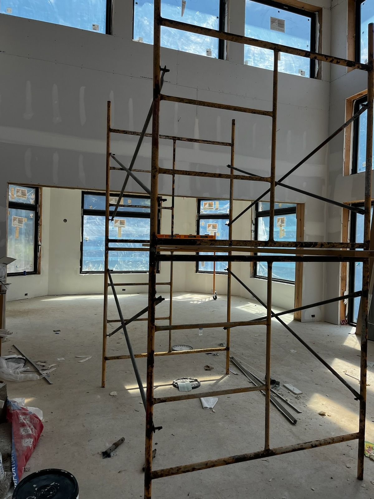 Scaffolding in an unfinished room with windows and drywall; construction in progress.