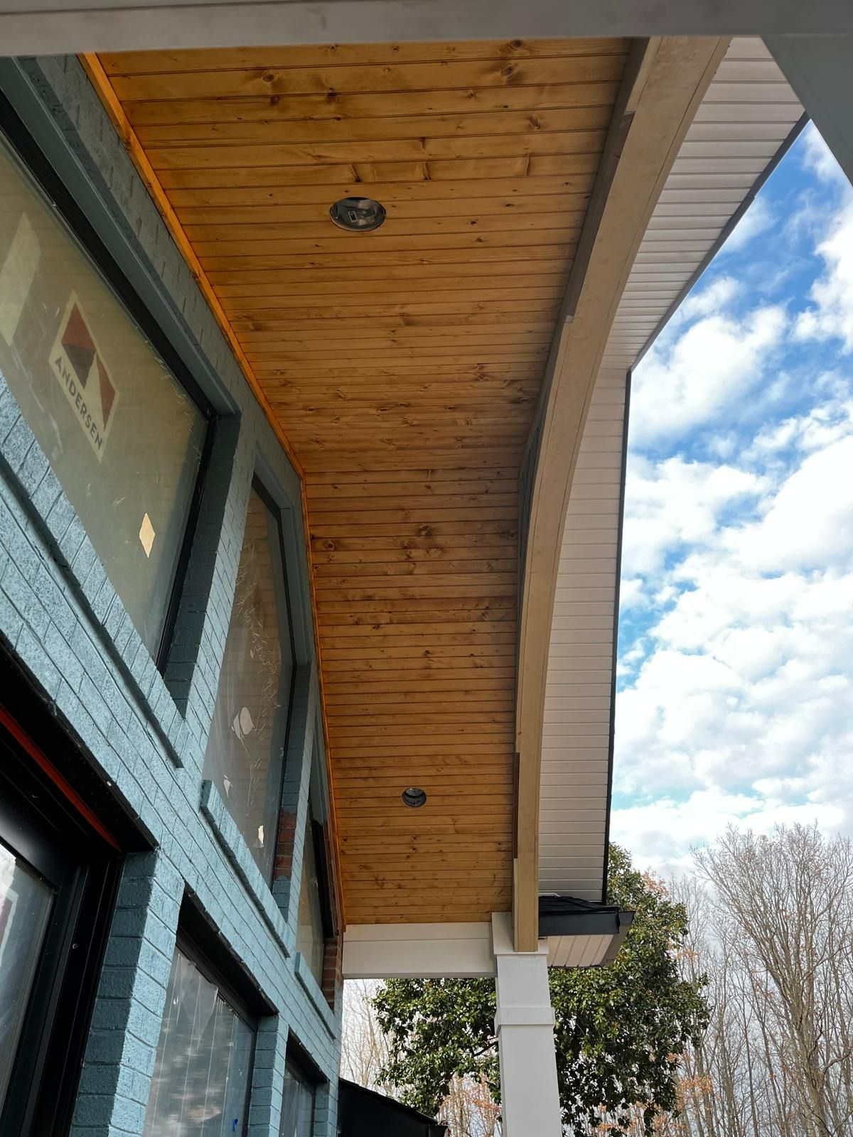 Wooden ceiling with recessed lights, blue trim, and a partly cloudy sky.