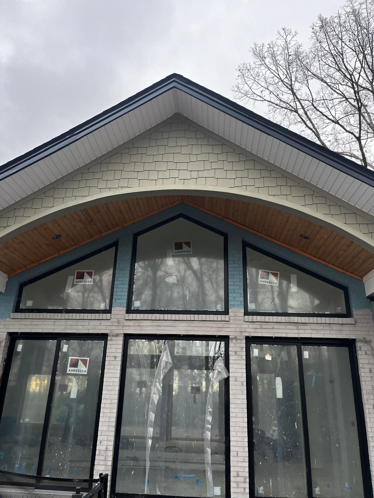 Exterior of a house with large windows, blue siding, white trim, and a wooden arched ceiling.