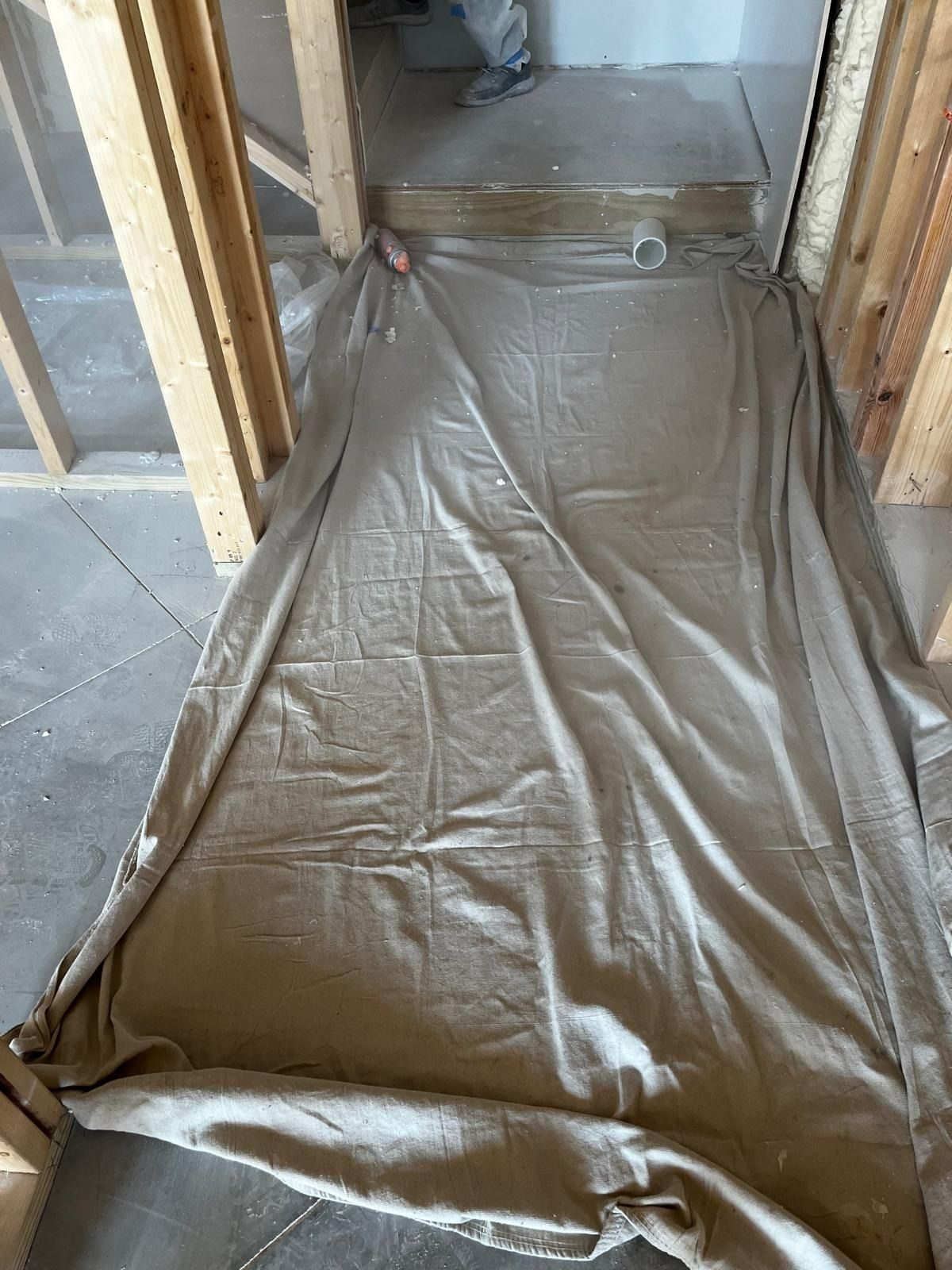 Beige tarp covers a concrete floor between wooden wall frames in a construction zone.
