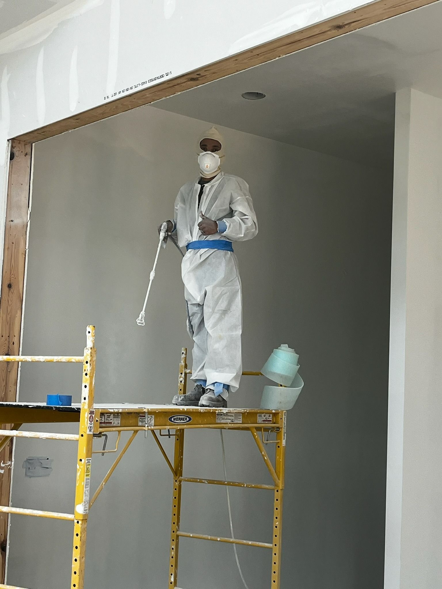 Man in protective suit sprays paint from scaffold in doorway.