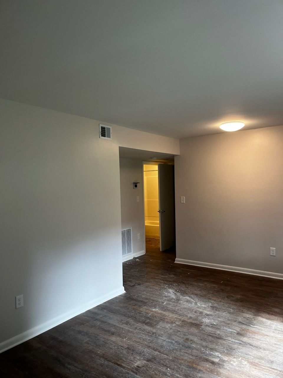 Empty room with wood-look floor, off-white walls, and a doorway leading to a brighter lit hallway.