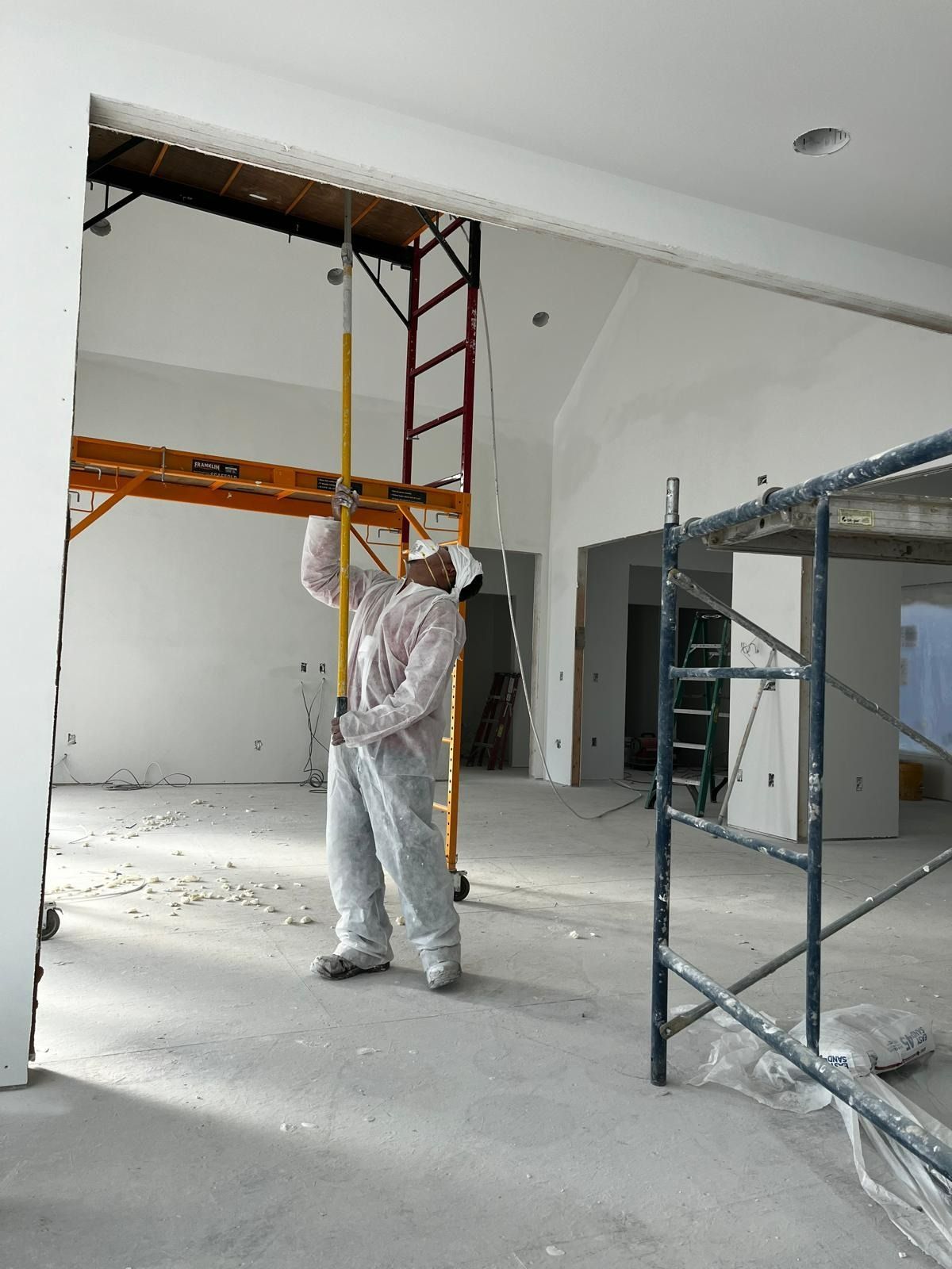 Man painting a high ceiling, using a long pole, standing near scaffolding in a construction site.