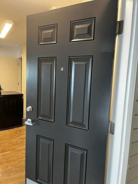 Black door with decorative panels, silver handle, and peephole, in an apartment entry.