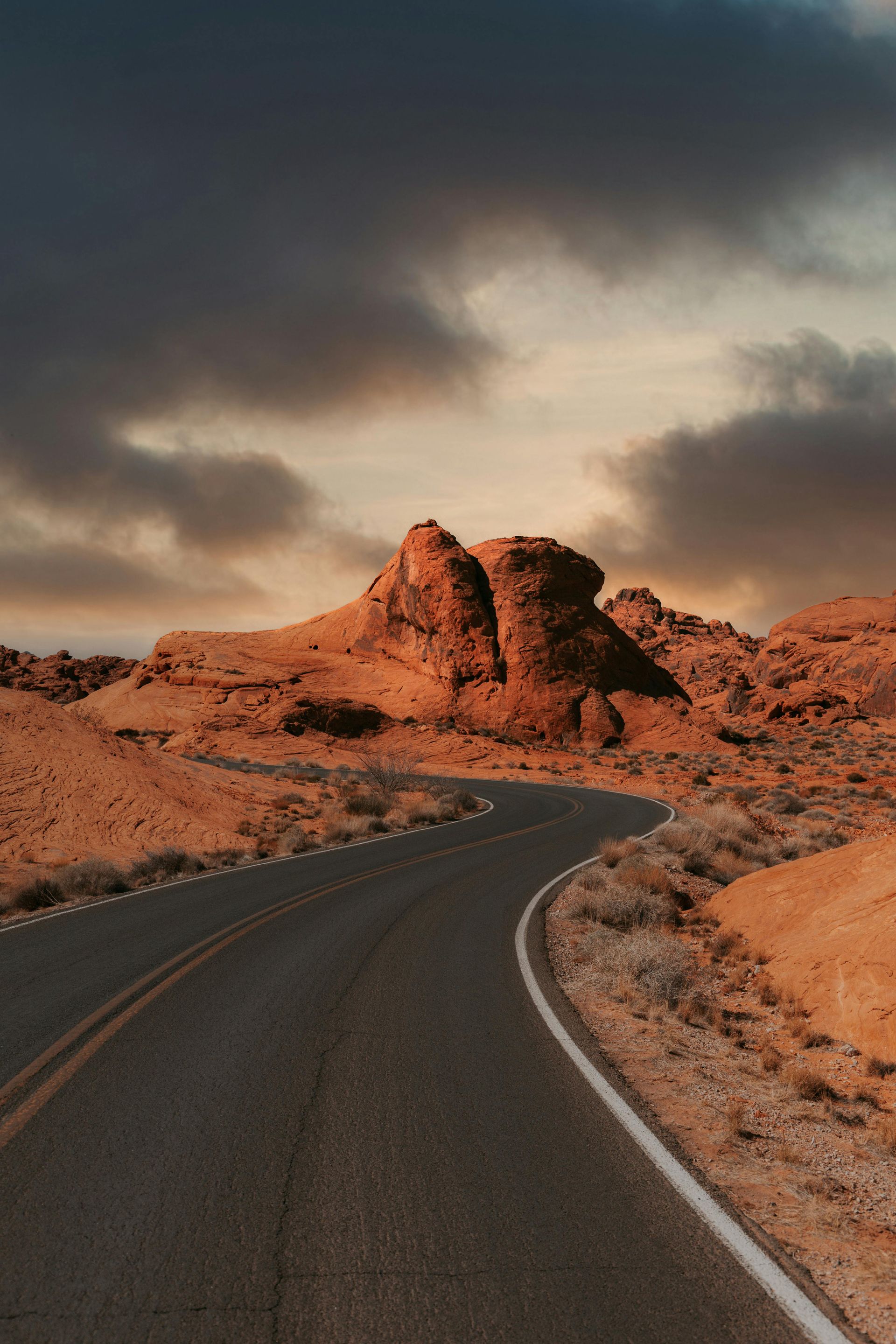 Winding desert road through red rock formations under a cloudy sky.