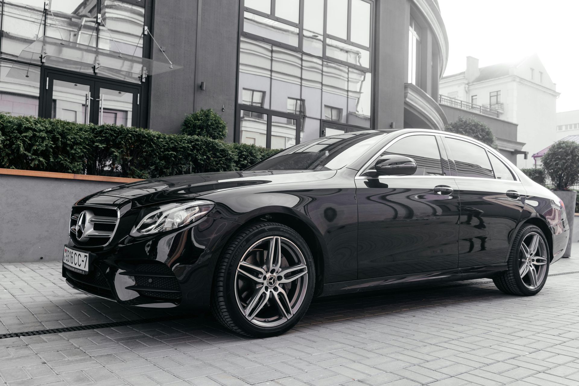 Black Mercedes-Benz sedan parked in front of a modern building with large windows.