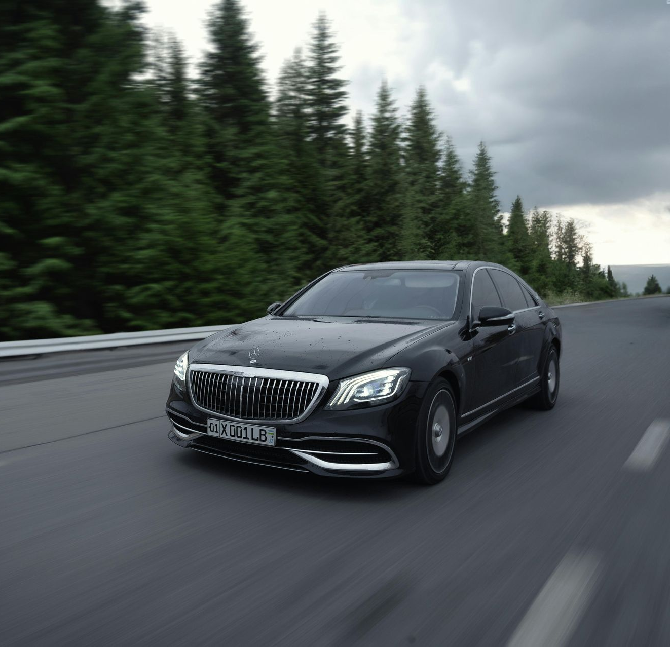 Black luxury sedan driving on a road, with trees in the background.