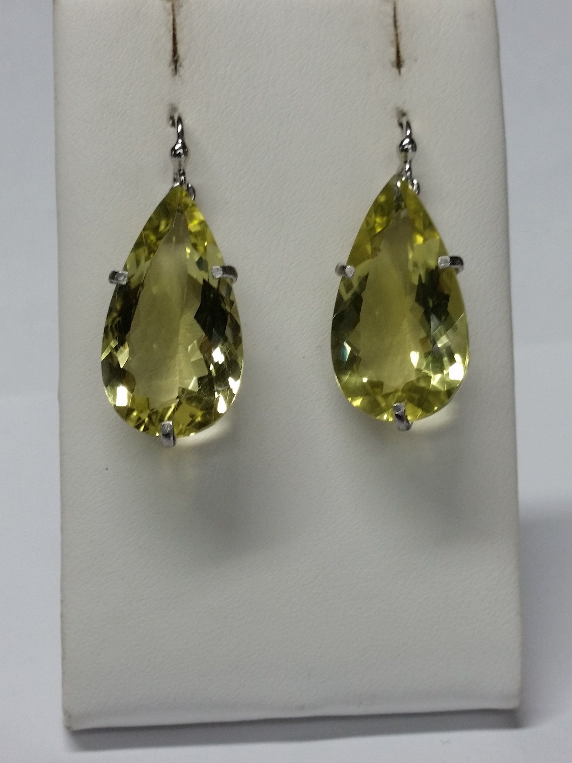 Un paio di orecchini pendenti a forma di pera con pietre preziose gialle, esposti su un supporto bianco.