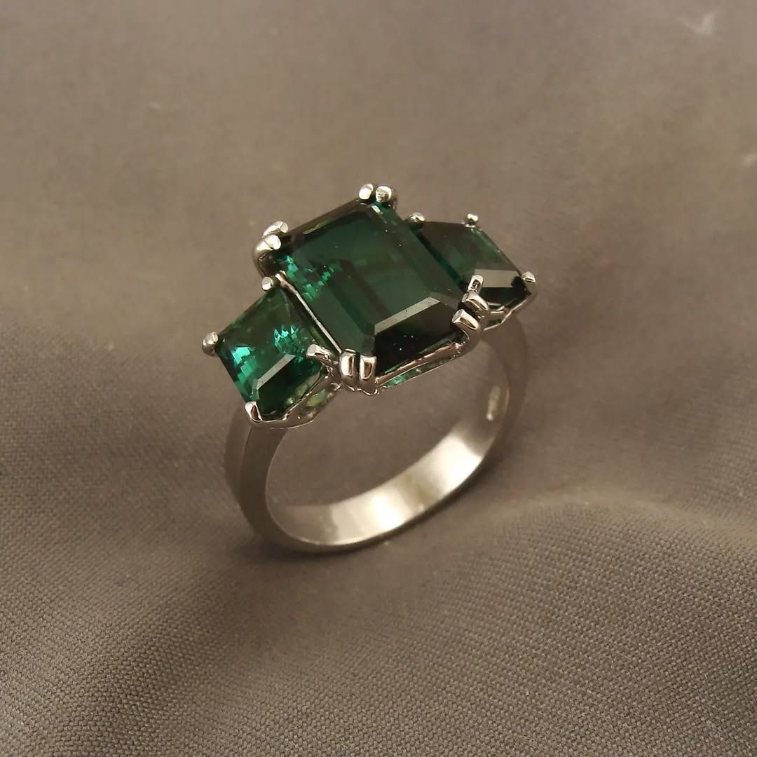 Anello in argento con una grande gemma verde centrale a taglio smeraldo, affiancata da due gemme verdi più piccole, anch'esse a taglio smeraldo.