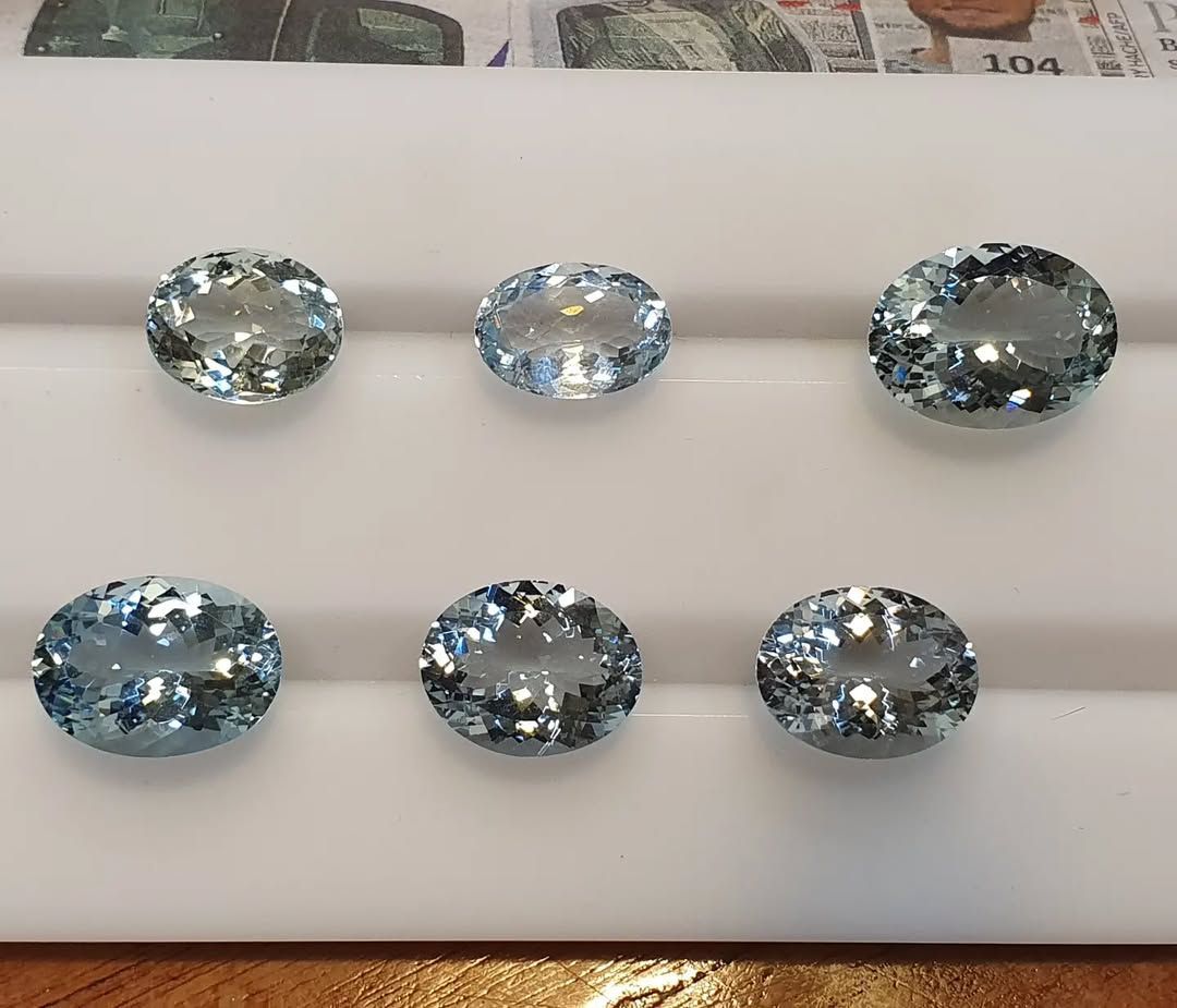 Sei gemme scintillanti di colore azzurro pallido, di forma ovale, disposte in due file su un vassoio bianco.