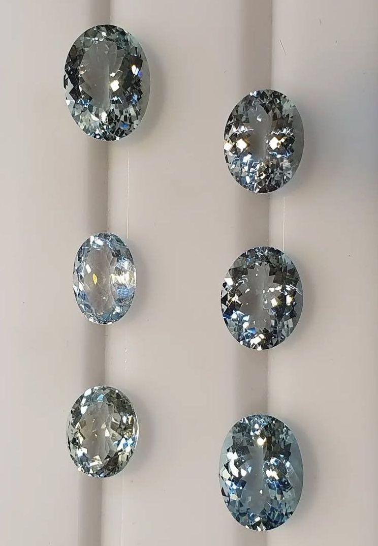 Sei gemme ovali di colore azzurro pallido, disposte in due colonne verticali su una superficie bianca scanalata.