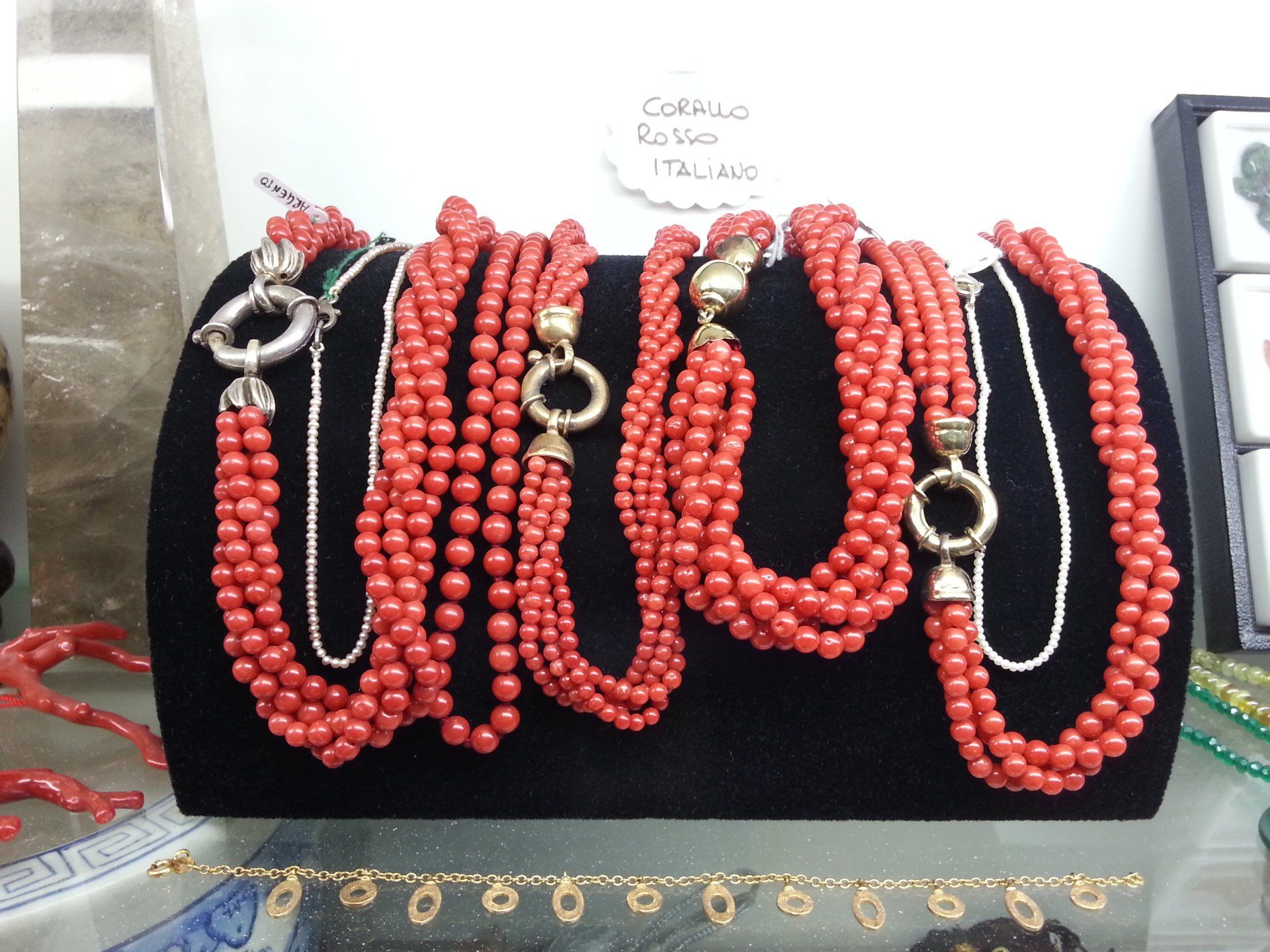 Diverse collane a più fili di perle di corallo con chiusure color oro, esposte su un supporto di velluto nero.