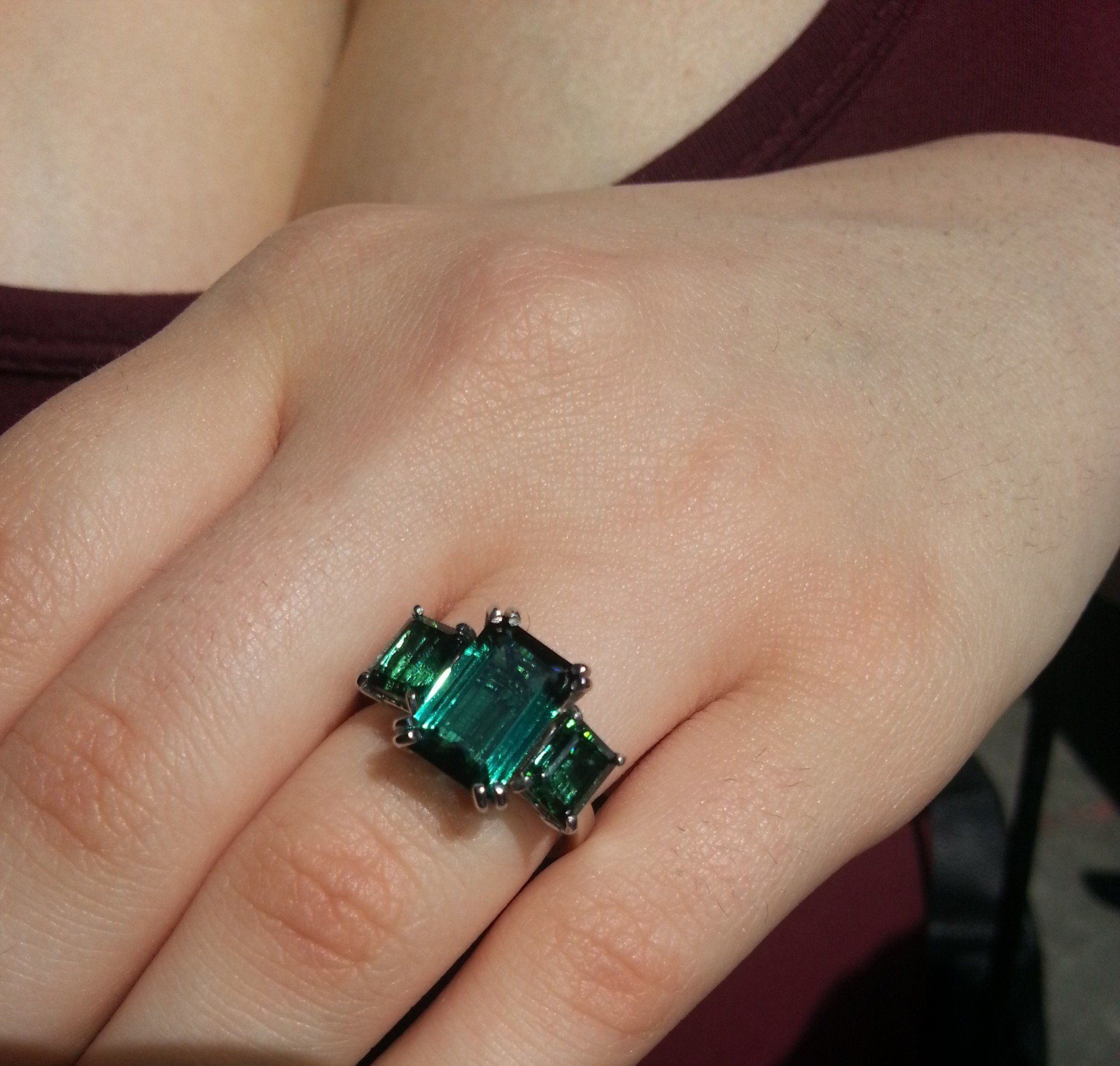 Primo piano di una mano che indossa un anello d'argento con una grande gemma verde a taglio rettangolare affiancata da due gemme più piccole.
