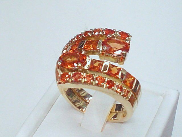 Anello in oro dal design curvo e a più file, impreziosito da numerose gemme arancioni di taglio rotondo e ovale su una base bianca.